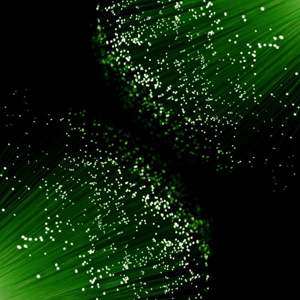 Close up capturing the ends of many illuminated green fibre optic light strands arranged against black.